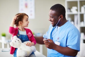 Happy male doctor communicating with child in clinic